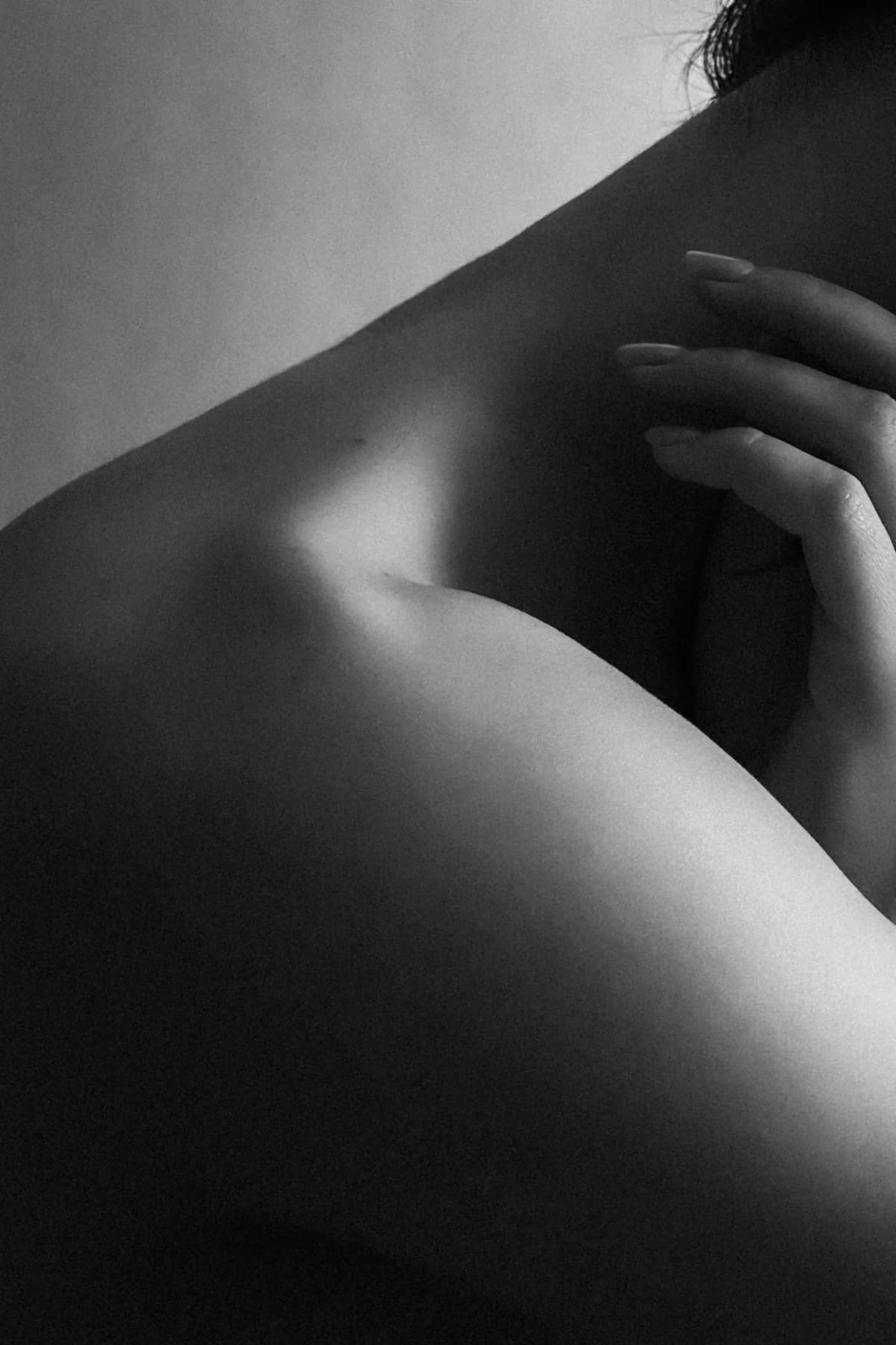 A hand resting on a bare shoulder, the neck turned away, in soft monochrome light